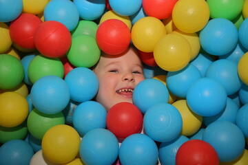 Fototapeta na wymiar A cheerful girl is playing in the playroom in the pool with balls of different colors