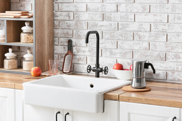 Wooden counter with ceramic sink, apples and coffee maker near light brick wall in kitchen