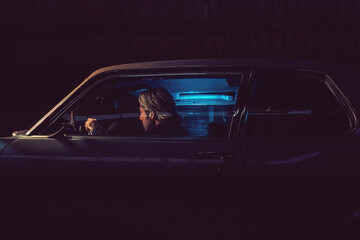 Man with blond hair sits inside an American classic muscle car at night.