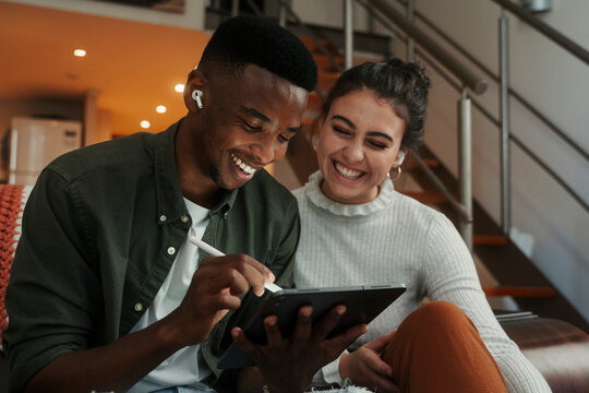 Biracial couple sitting on sofa writing on digital tablet