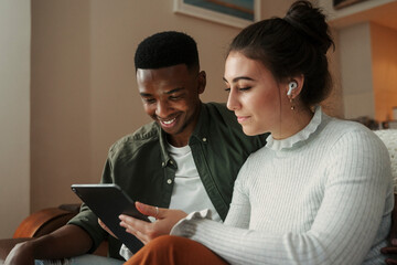 Biracial couple sitting on sofa scrolling on digital tablet 