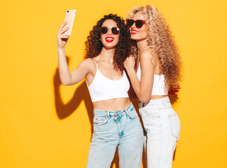 Two beautiful sexy smiling hipster women in summer clothes.Trendy models with afro curls hairstyle...