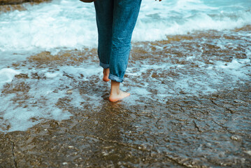 woman walking by rocky beach barefoot wet jeans