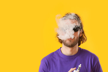 Vaping young man on yellow background