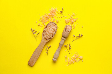 Composition with wooden spoon and scoop of sea salt on yellow background