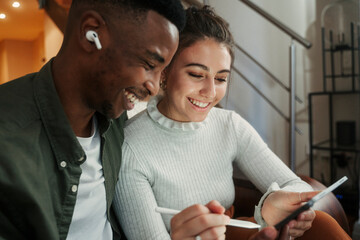 biracial couple sitting on sofa drawing with pen on digital tablet  - Powered by Adobe