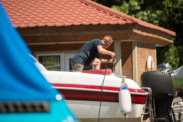 A man washes a motor yacht with a jet of water at a boat station
