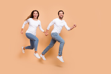 Fototapeta na wymiar Full length body size view of attractive cheerful partners jumping motion holding hands isolated over beige pastel color background