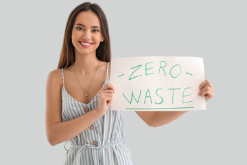 Young woman holding paper sheet with text ZERO WASTE on light background