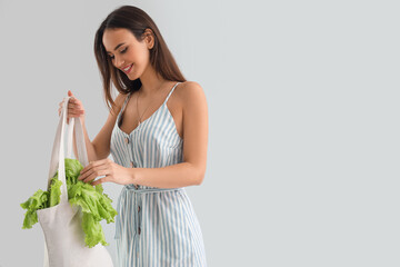 Young woman with shopping bag and lettuce on light background