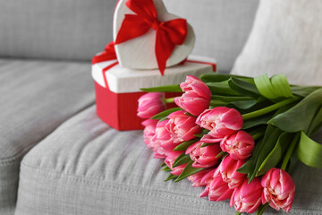 Bouquet of tulip flowers with gifts on sofa