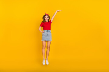 Full body photo of cute small girl jump high wear red t-shirt hairband jeans skirt sneakers isolated on yellow background