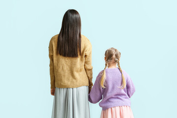 Little girl and her mother in warm sweaters holding hands on light background