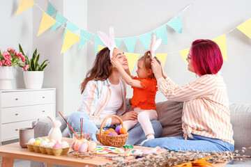 Young lesbian couple with little daughter during painting of Easter eggs at home