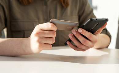 Woman hands closeup holding credit card and phone. Woman sitting at table and paying in application, shopping online or doing bank transaction. High quality photo