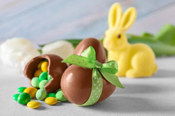 Chocolate Easter eggs with bow and candies on light background