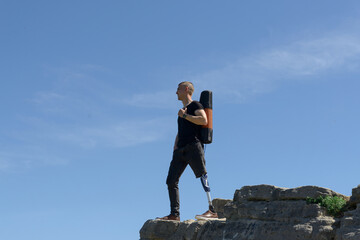 a man on a prosthetic leg travels the mountains. Dressed in black jeans and a T-shirt, he carrying...
