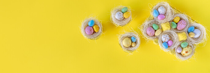 Happy Easter concept. Sweet bright easter eggs in nests on yellow background