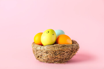 Nest with funny Easter eggs on color background