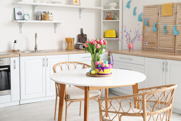 Basket with Easter eggs, vase and tulips on dining table in kitchen