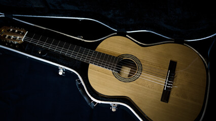 The classical guitar lies in an open black trunk. Flamenco guitar in a trunk on a dark background....