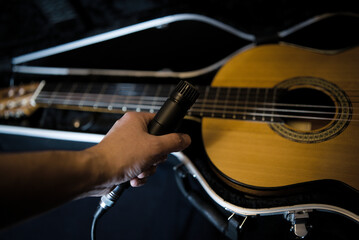 Naklejka premium A hand holding a dynamic microphone against the background of an open trunk with a guitar lying in it. A classical guitar in a black trunk and a black microphone in the performer's hand. Accessories o