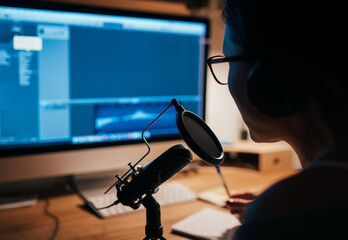 Microphone with pop filter closeup photo with a young woman in headphones recording voice using a...