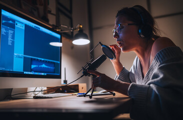 Young woman in headphones recording vocal voice using microphone with pop filter and desk top computer. Home sound studio Modern audio recording technology concept image.