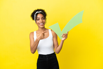 Young african american woman isolated on yellow background holding a check icon and pointing it