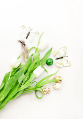 Spring Easter holiday white background with tulips, quail eggs, butterflies and feathers. Top view