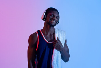 Attractive young black guy with towel listening to music in headphones in neon lighting