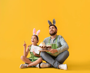 Little girl, her father with Easter cakes and greeting card on yellow background