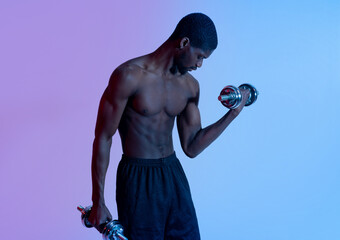 Strength training concept. Young black guy with sexy body exercising with dumbbells, pumping up muscles in neon light
