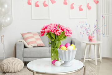 Vase with tulips and Easter eggs on table in living room