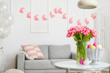 Vase with tulips and Easter eggs on table in stylish living room interior