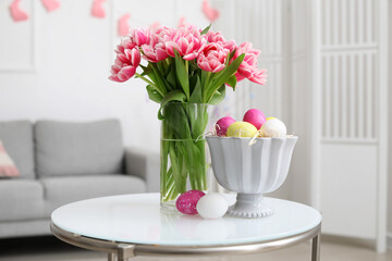 Vase with tulips and Easter eggs on table in room