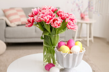Vase with tulips and Easter eggs on table in room