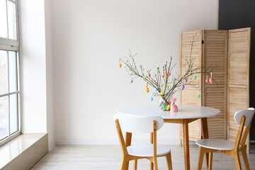 Tree branches decorated with Easter eggs in vase and rabbit on dining table in light room