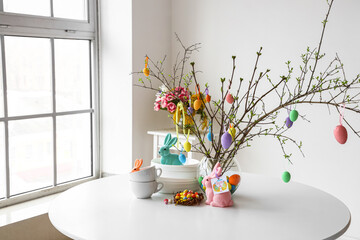 Dishware and tree branches decorated with Easter eggs on dining table in room