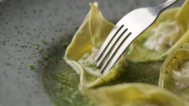 Fork impales Chinese wonton dumplings on gray plate close up. Asian traditional soup with wontons, stuffed with meat. Stuffed steam dumplings dim sum handmade. Restaurant Chinese cuisine. Slow motion.