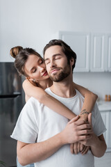 tattooed young woman hugging bearded man in white t-shirt.
