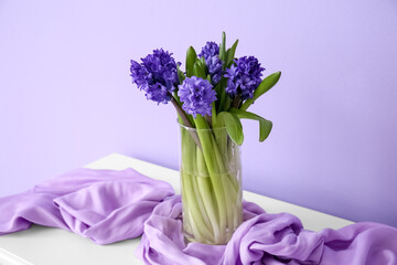 Vase with hyacinth flowers on table near color wall