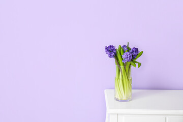 Vase with hyacinth flowers on table near color wall