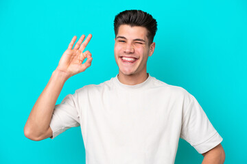 Young handsome caucasian man isolated on blue bakcground showing ok sign with fingers