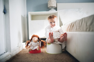 Cute caucasian kid with doll sit on potty in bedroom, concept of hygiene and potty training