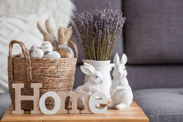 A wicker basket with Easter eggs, lavender, candles and white rabbits in the interior of the living...