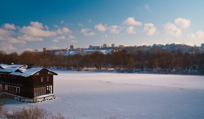Winter landscape on a frosty sunny day. An old wooden house on a barge in the middle of a frozen river. A snow-covered, frozen river with an old house on the pier