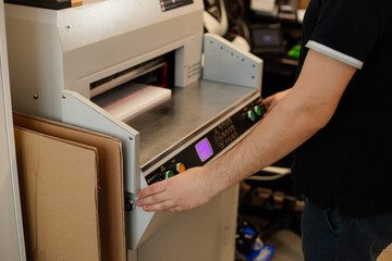 Cropped image man hands using paper cutter machine, guillotine offset. Control panel,set up laser...
