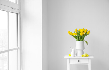 Vase with yellow tulips, Easter eggs and rabbit on table near light wall