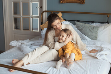 Loving mom and baby girl with glitter on cheeks smiling nad hugging at domestic living room with modern interior. The concept of a happy relationship between mother and daughter. Happy mothers day